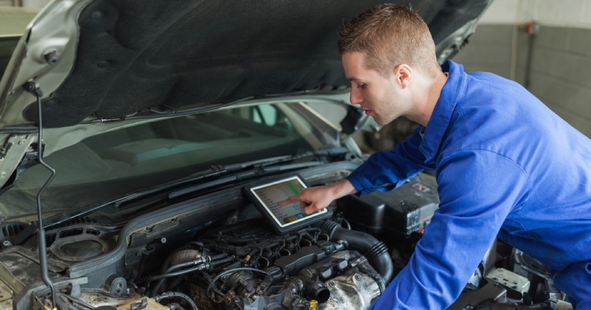 Male mechanic with digital tablet repairing car engine